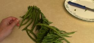 After making a knot, insert the green beans into the thread using the needle